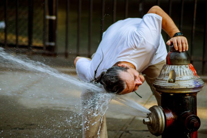 A strong heat temperature and the man is refreshed with water from a fire hydrant